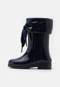 Botte de pluie en caoutchouc imperméable bleu marine avec une finition brillante, bout rond et un revers sécurisé par un ruban en satin en haut.