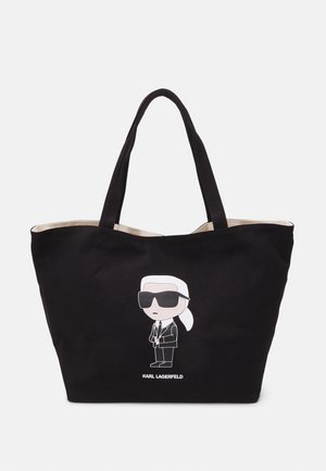 Sac cabas noir avec de longues anses et un personnage de dessin animé portant des lunettes de soleil et un costume, étiqueté "Karl Lagerfeld" sur le devant.