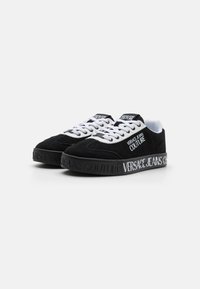 Svarte semskede sneakers med hvite snøringer og gummisåle. Har preget merkevare på sålen og tungen. Klassisk lavtopp-design.