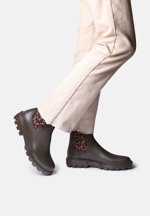 Brown rubber ankle boots with a textured leopard-print panel, featuring a chunky sole and elastic side for easy wear. Paired with light-colored trousers.