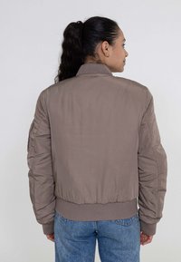 Giacca marrone stile puffer con polsini e colletto a costine. Presenta una superficie liscia e una forma leggermente oversize. Senza loghi o decorazioni visibili.