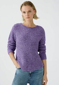Lila Strickpullover mit geripptem Muster, weitem Halsausschnitt und langen Ärmeln. Kombiniert mit hellblauen Jeans.