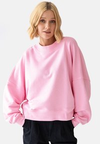 Oversized różowy sweatshirt z prążkowanym okrągłym dekoltem i szerokimi rękawami, wykonany z miękkiej tkaniny o gładkiej fakturze.