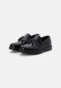 Mocassins en cuir noir avec une finition lisse, présentant un accent décoratif de glands sur le dessus, et une semelle en caoutchouc texturée pour l'adhérence.