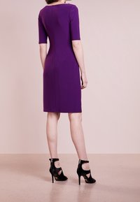 Lila, knälång klänning med korta ärmar, figurnära design, slät tyg. Bärs med svarta klacksandaler med vristremmar.