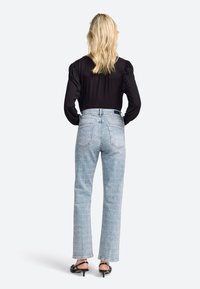Vaqueros de tiro alto de color azul claro con un patrón desvaído, piernas rectas y bolsillos traseros, combinados con una blusa negra de manga larga y tacones negros.