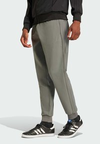 Gray athletic pants with ribbed cuffs and side zippers, featuring subtle branding. Paired with black shoes with white stripes and blue accents.