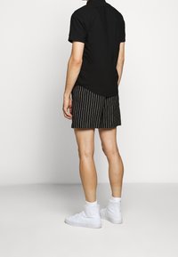 Svart kortärmad skjorta, randiga svart och vita shorts, och vita högklackade sneakers, sedd från baksidan.