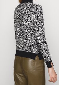 Pull imprimé léopard noir et blanc avec un col haut, des poignets noirs côtelés et des fentes latérales ; associé à un pantalon en cuir vert olive.