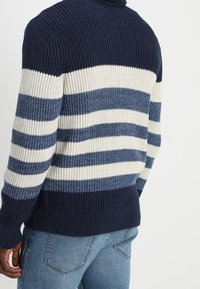 Marineblau- und cremefarbener gestreifter Pullover mit gerippter Textur, der horizontale Streifen und einen taillierten Saum aufweist. Dicke Strickware, Rundhalsausschnitt.