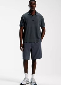 Mörkgrå pikétröja med vita detaljer, kombinerad med mörka shorts och ljusgrå sneakers. Tyget har ett strukturerat mönster.