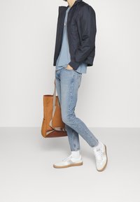 Námořnicky modrá bomber bunda, světle modré tričko, svetle prošité džíny, bílé tenisky s béžovými podrážkami, oranžový batoh s béžovými detaily.