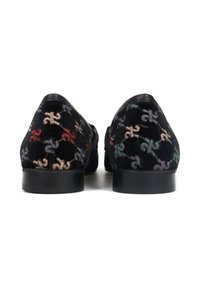 Para czarnych aksamitnych loafersów z wielokolorowymi haftowanymi wzorami fleur-de-lis, pokazane od tyłu na białym tle.