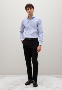 Camicia a righe blu e bianche con bottoni abbinata a pantaloni neri e scarpe nere. La camicia ha maniche lunghe e colletto.