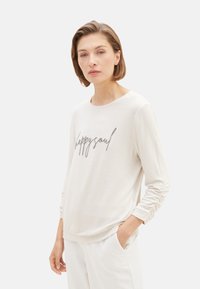 Hellbeige Langarmshirt mit dem Aufdruck "happy soul" in silberner Schrift. Weicher Stoff, lockerer Schnitt und geraffte Details an den Ärmelbündchen.