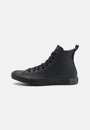 Black high-top sneaker with a canvas upper, rubber toe cap, and lace-up closure. Features a textured surface and a reinforced heel.