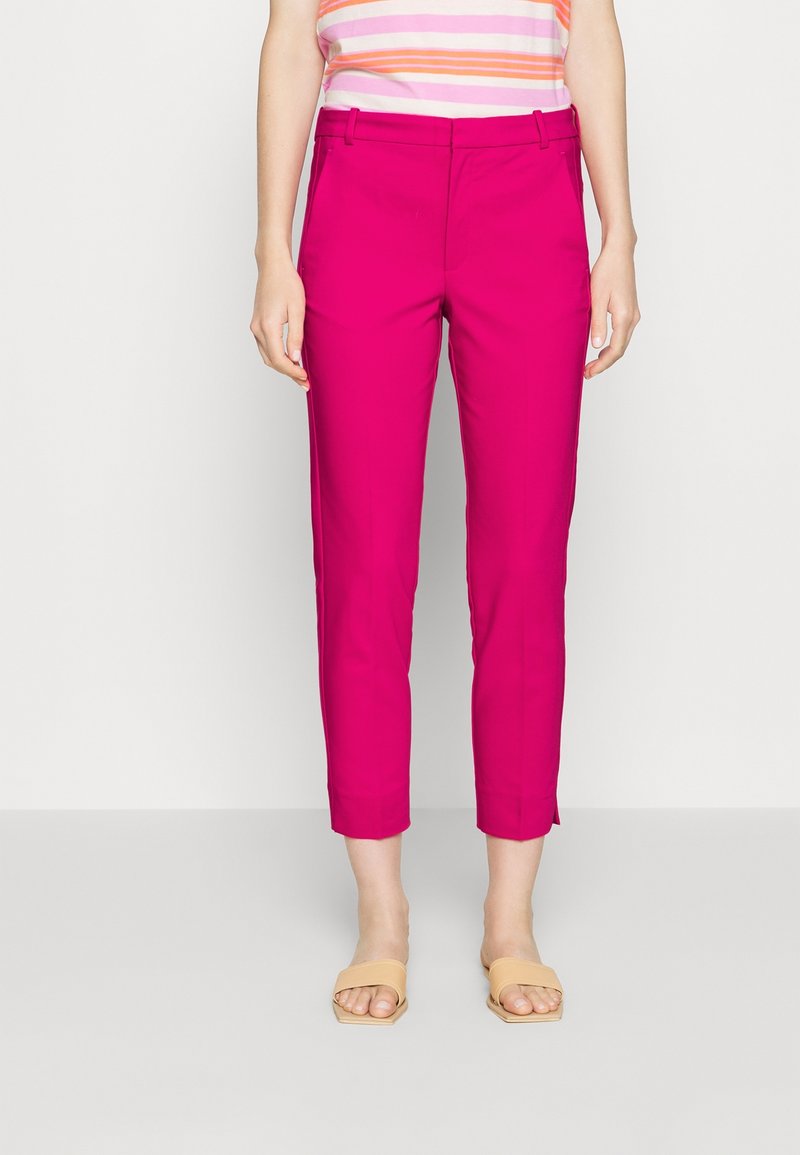 Femme portant un pantalon fuselé rose vif jusqu'aux chevilles, des sandales beige à bout ouvert et un haut sans manches à rayures roses et blanches.