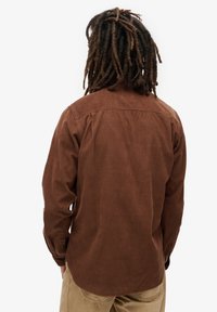 Bruine ribfluwelen blouse met lange mouwen, puntkraag en knoopmanchet. Soepele textuur, rechte snit en afgeronde zoom.