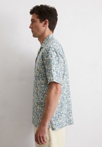 Korte mouwen shirt in lichtblauwe katoen, met een bladerenpatroon in crème. Ontspannen pasvorm met een camp-kraag, knoopsluiting aan de voorkant en zijsplitten.