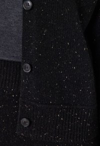 Cardigan nero a maglia con una finitura texture, caratterizzato da macchie bianche e bottoni neri lungo la parte anteriore. Polsini e orlo a costine.