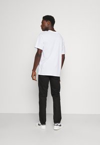 Camiseta blanca de algodón con cuello redondo, combinada con pantalones negros y zapatillas blancas con detalles en negro. Costuras visibles y diseño sencillo.