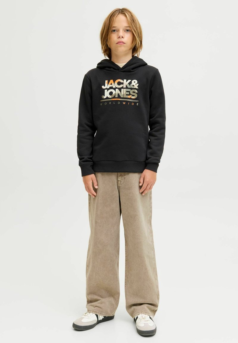 Felpa nera con logo "JACK & JONES" in colori metallici, abbinata a pantaloni larghi beige e scarpe da ginnastica nere e bianche.