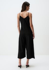 Zwarte jumpsuit van lichtgewicht stof, met een V-nek, dunne bandjes en wijd uitlopende cropped pijpen. Minimalistisch ontwerp zonder zichtbare patronen.