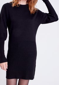Abito nero in maglia con texture a coste, maniche lunghe e vita aderente. L'abito presenta un delicato gradiente da tessuto liscio a tessuto a coste.