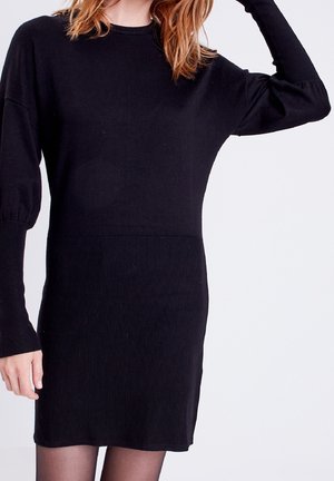 Robe noire en tricot avec une texture côtelée, des manches longues et une taille cintrée. La robe présente un dégradé subtil entre un tissu lisse et un tissu côtelé.