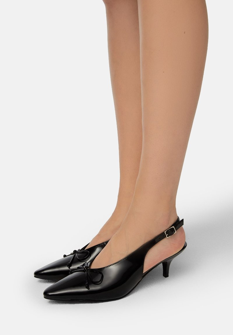 Melna patentēta ādas slingback papēža kurpes ar smailu purngalu, ar priekšējo loku detaļām un slaidu kaķīša papēdi. Gluda, spīdīga apdare.