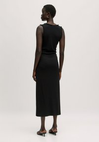 Zwarte, mouwloze ribbenjurk met gerimpelde schouderaccenten. Lange, aansluitende stijl die onder de knieën reikt. Gladde textuur en minimalistische uitstraling.