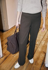 Tmavě hnědé kalhoty s širokými nohavicemi a jemnou texturou, zkombinované se šedým svetrem a hnědou koženou taškou. Celý look doplňují bílé tenisky.