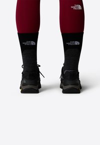 Black athletic shoes with gray accents, worn with dark gray and black socks, paired with burgundy leggings featuring a logo.