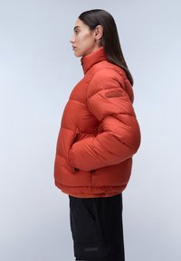 Rode pufferjack met een hoge kraag, geborduurd ontwerp en zijzakken. Beschikt over elastische manchetten en een zoom voor een aansluitende pasvorm.