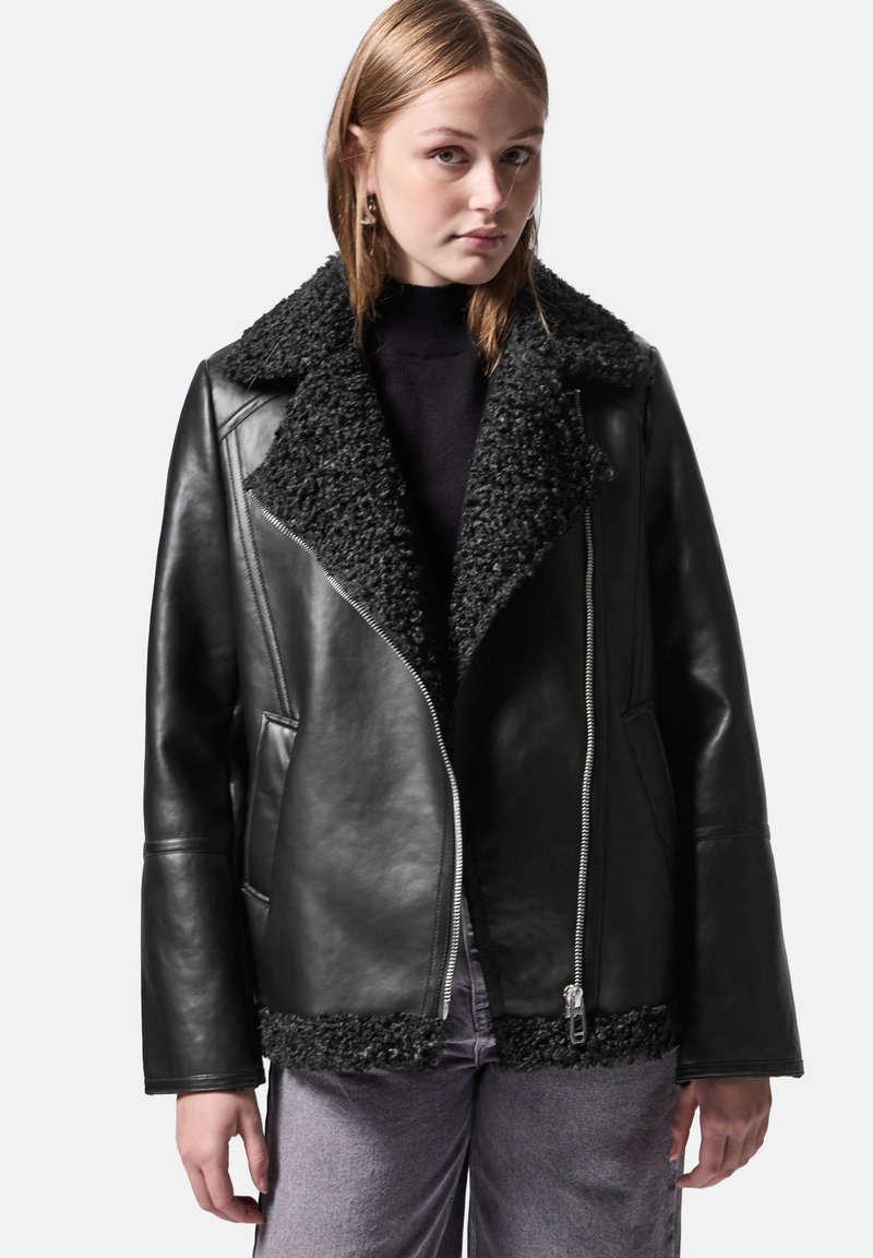 Giubbotto di pelle nera con un colletto e orlo in shearling nero morbido e texturizzato. Presenta una chiusura con zip e tasche laterali, vestibilità su misura e maniche affusolate.