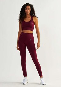 Bordowy stanik sportowy i legginsy o wysokim stanowiące z teksturowanego materiału, z małym akcentem logo. Buty w białym sportowym stylu.