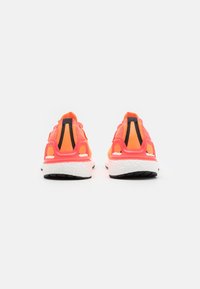 Neon oranžové sportovní boty s černými akcenty a bílými podrážkami. Mají texturovaný svršek a polstrovanou patu pro podporu.
