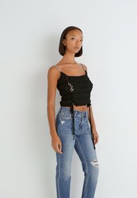 Black cropped top with textured knit, adjustable lace-up sides, and silver chain straps, paired with medium-wash distressed jeans.
