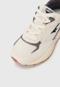 Sneaker beige clair avec des matériaux en maille et en daim. Présente un col rembourré, des accents gris et une semelle épaisse et texturée avec une semelle extérieure en caoutchouc gomme.
