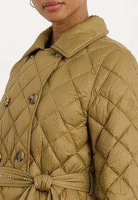 Gequilte olijfgroene pufferjack met een dubbelgebreid ontwerp, grote knopen, een ceintuur in de taille en een hooguitgevoerd logo op de borst.