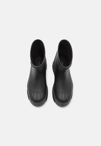 Botas de tobillo de goma negra con una textura suave, punta redondeada y detalles acanalados en la punta y la suela. Plantilla plana visible en el interior.