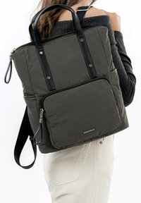 Sac à dos matelassé gris avec poignées et fermeture éclair en cuir noir. Doté d'une poche avant et d'une sangle réglable. Tissu texturé avec un léger éclat.