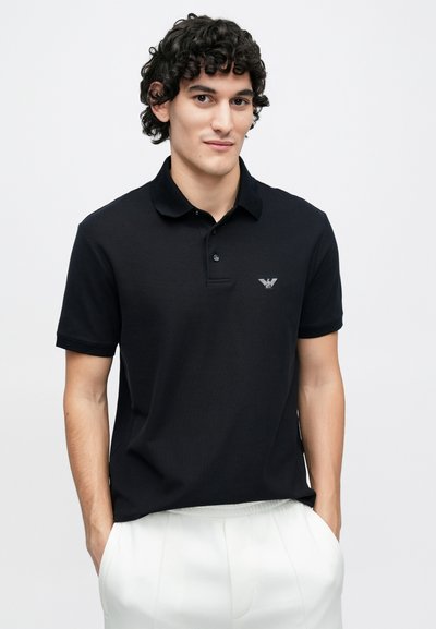 Čierne polo tričko z textúrovaného materiálu s gombíkmi na légach a krátkymi rukávmi. Na hrudi je vyšívané logo.