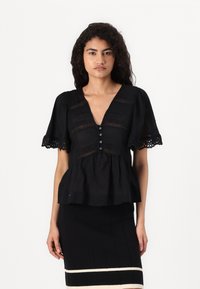 Svart peplum-bluse med korte pufferm, med dyp V-hals og intrikate spissdetaljer. Frontlukking med knapper og myk tekstur.