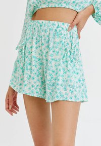 Jasnoniebieskie kwieciste szorty wykonane z miękkiego materiału, z elastycznym paskiem w talii, falbankami na krawędziach oraz rozsianym wzorem kwiatowym w różnych odcieniach zieleni.