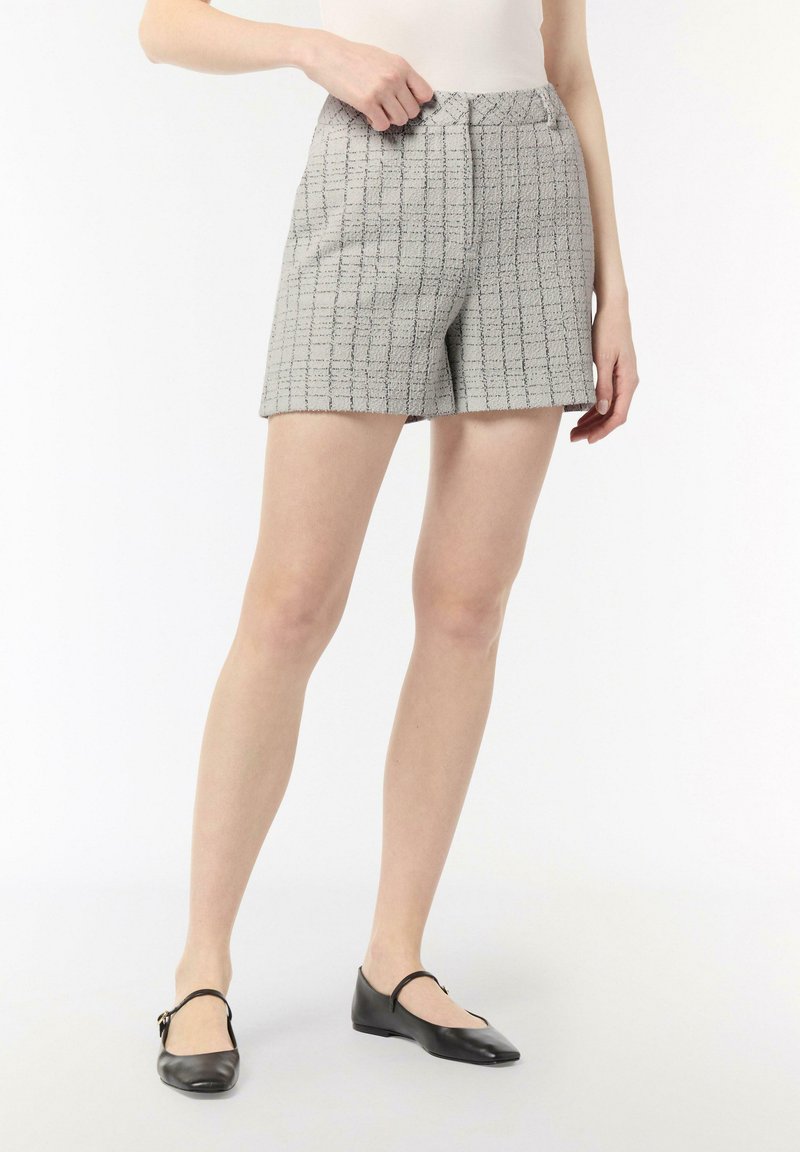 Graue Tweed-Shorts mit einem Karomuster, knielang, mit einem Bund und Seitentaschen. Kombiniert mit schwarzen Leder-Ballerinas.