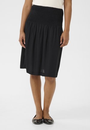 Černá sukně po kolena s nařaseným pasem a lehkou látkou; nošena s černými balerínkami, ukazující hladkou texturu a jednoduchý design.