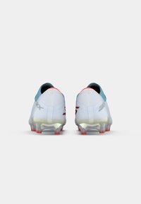 Botas de futebol brancas com um acabamento suave, detalhes em azul claro, calcanhar vermelho, sola transparente com pontas vermelhas e marcação prateada nos lados.