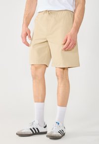 Shorts beiges en tissu lisse, dotés d'une taille �élastique avec cordon de serrage. Le design est de longueur genou avec des jambes droites.