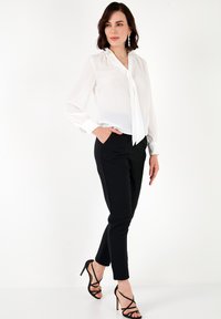 White blouse with a tie neck, sheer sleeves, and button cuffs paired with black fitted pants and strappy black high heels.